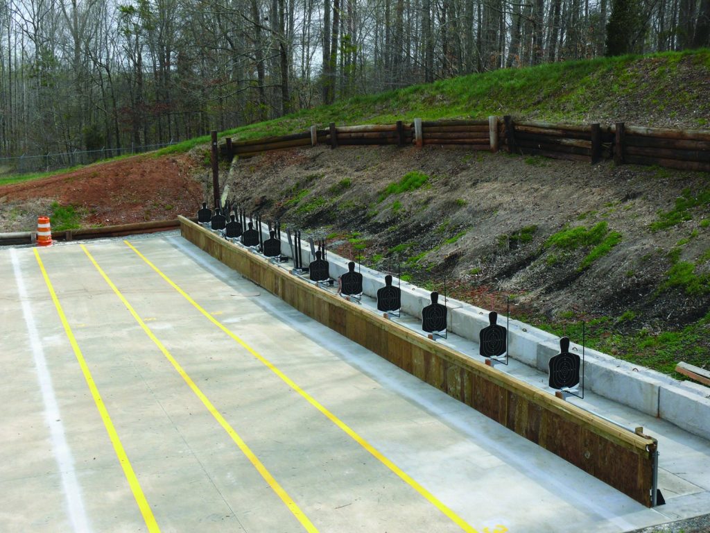 Targets lined up on a shooting range, with marked lanes and a wooded embankment behind.